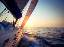 Sail boat gliding in open sea at sunset