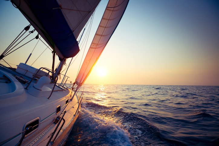 Sail boat gliding in open sea at sunset