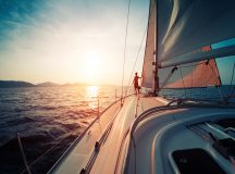 Young man standing on the yacht in the sea at sunset