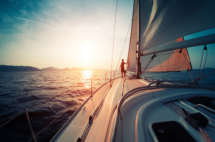 Young man standing on the yacht in the sea at sunset
